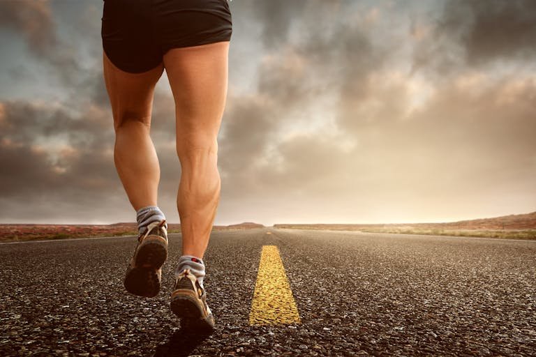 Runner's legs on a road during a sunset, symbolizing endurance and outdoor fitness training.